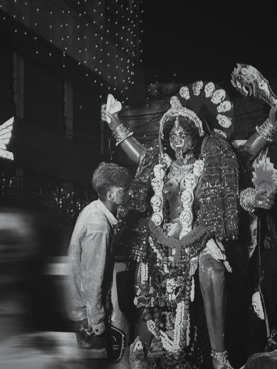 A black-and-white photograph of a person beside a decorated deity figure.