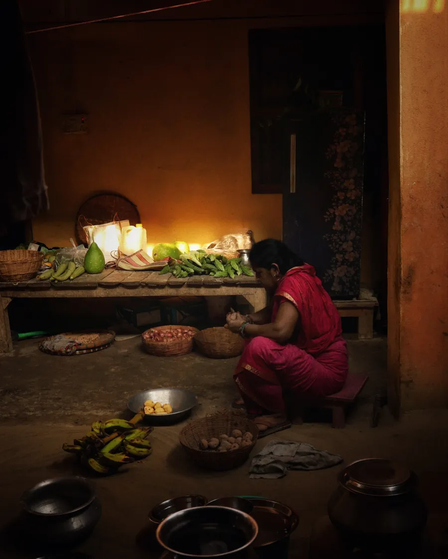 A person in red sits beside baskets, produce and metal vessels indoors.