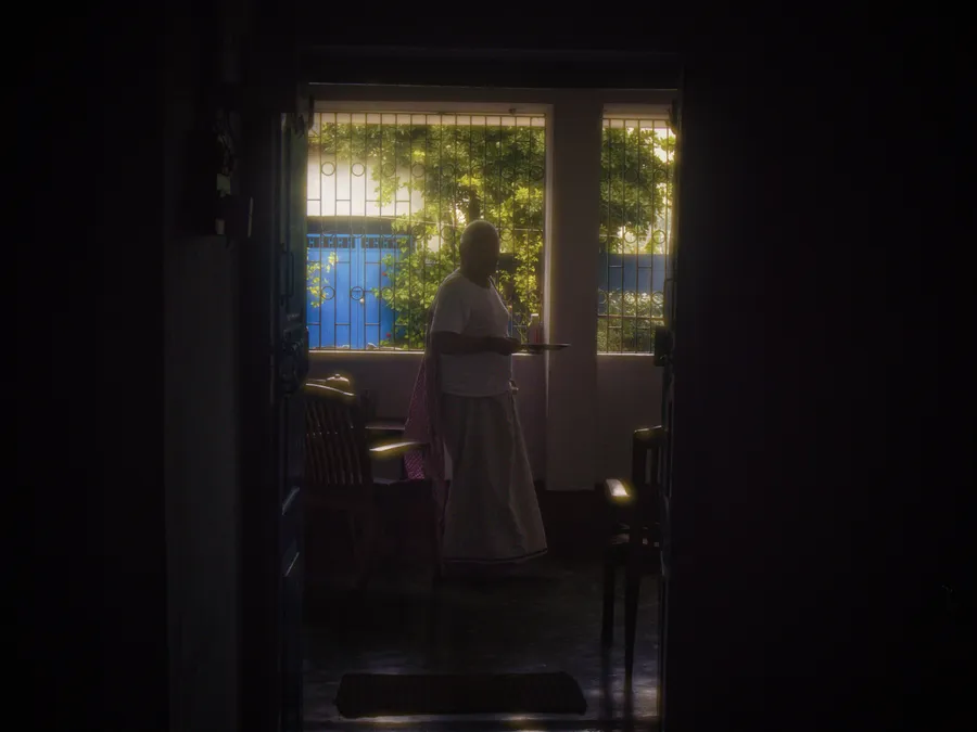 A person stands in a dark interior beside a bright doorway or window.