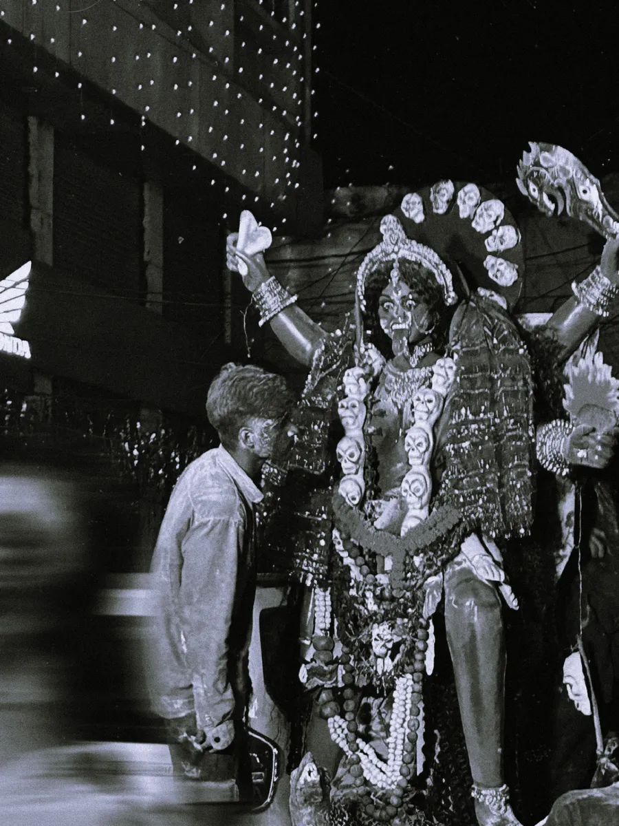 A black-and-white photograph of people beside a decorated deity figure.